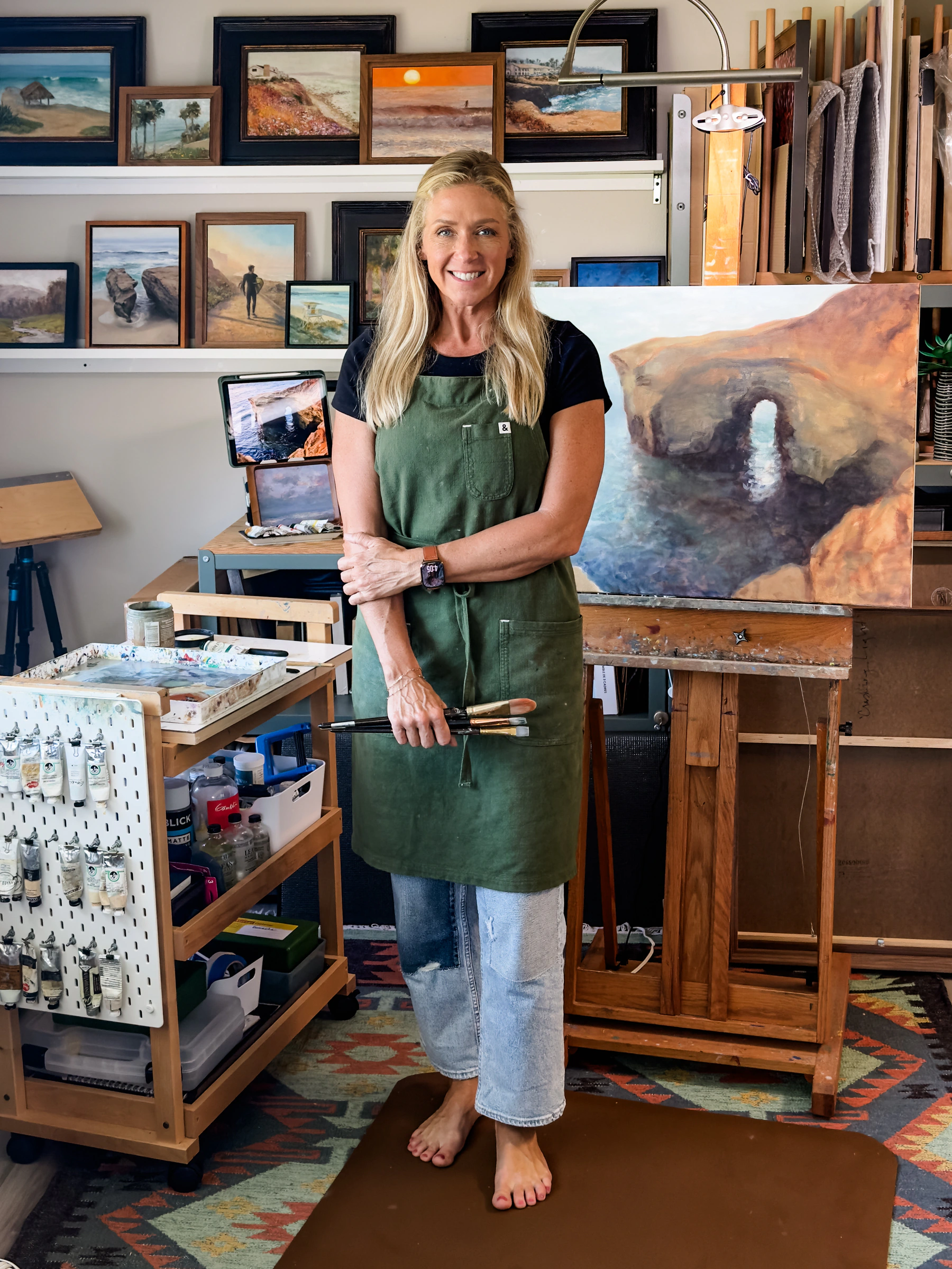 Jill Weeks Smith standing beside an original coastal arch painting in her studio