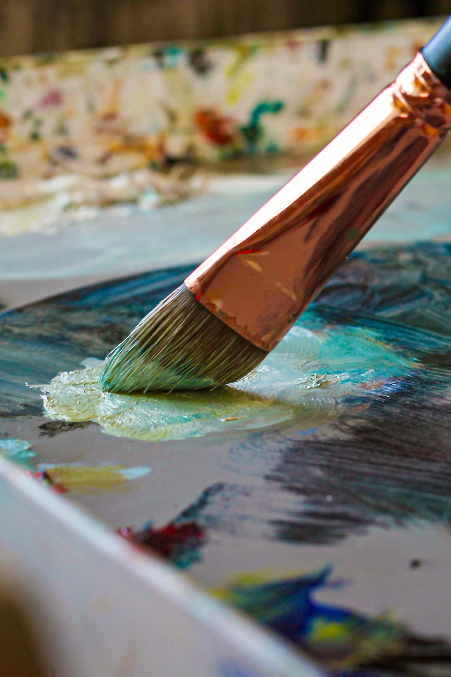 A brush mixing blue and green oil paint on Jill Weeks Smith’s palette
